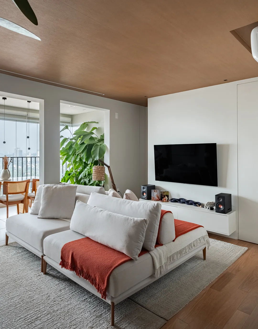 Sala com sofá claro, manta laranja e forro de madeira