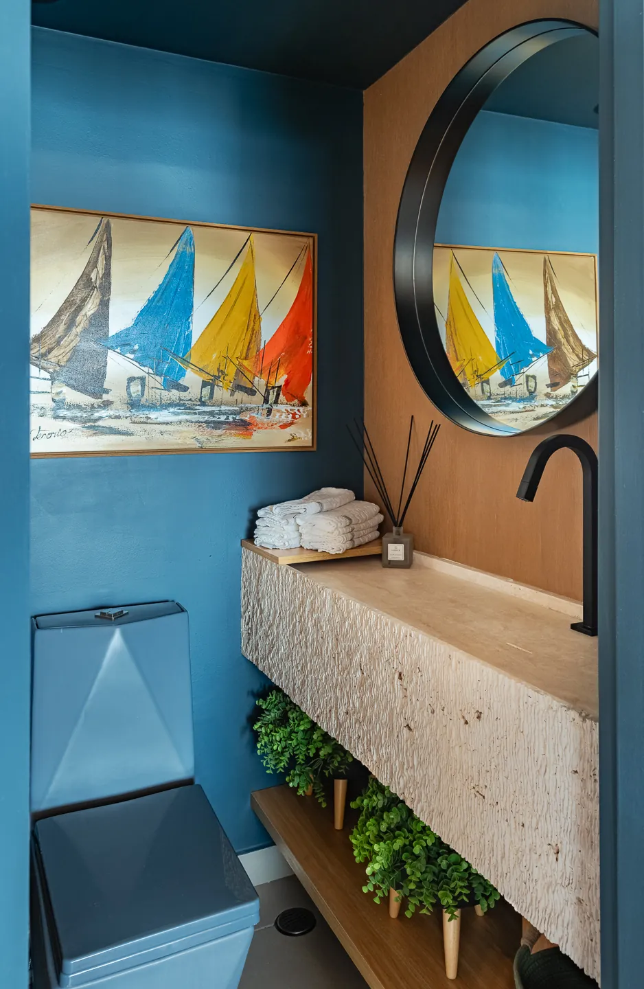 Lavabo com parede azul, bancada de pedra e quadro de veleiros