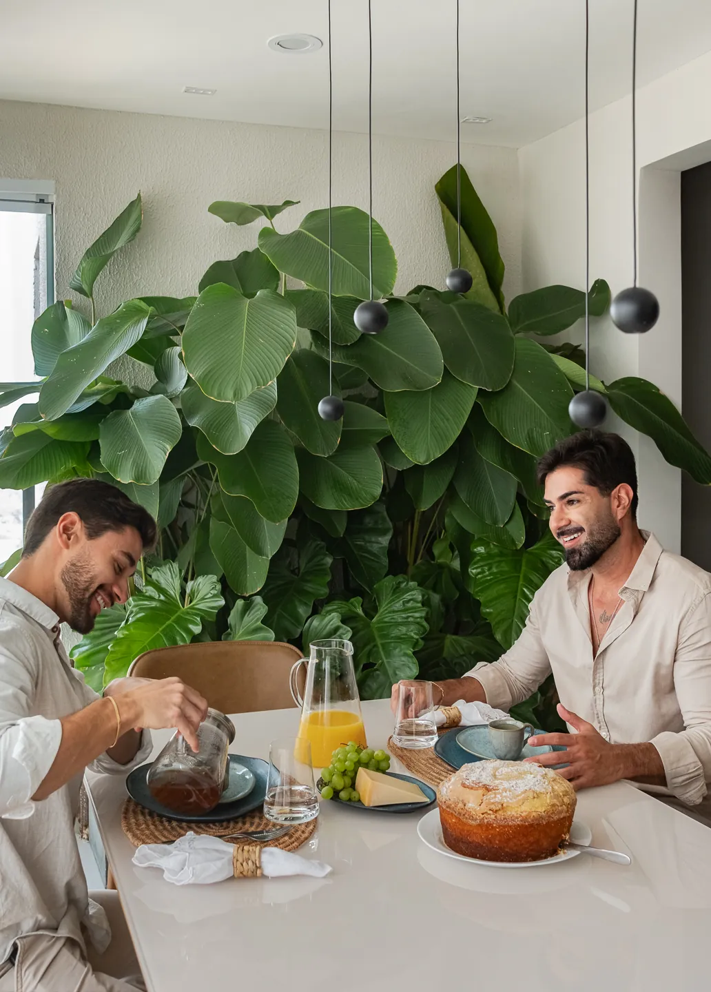 Moradores tomando café da manhã na mesa de jantar, com plantas ao fundo